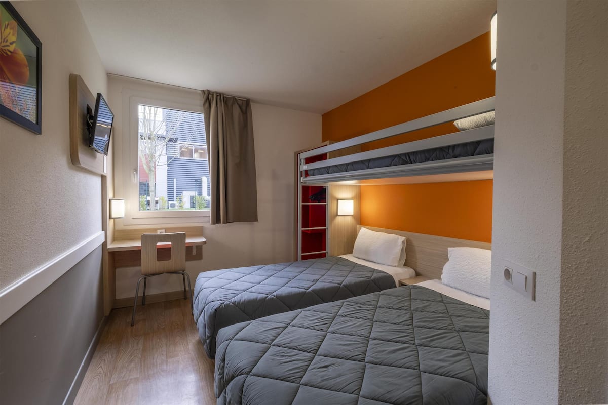 A compact room with two beds, a desk, and a window with curtains.