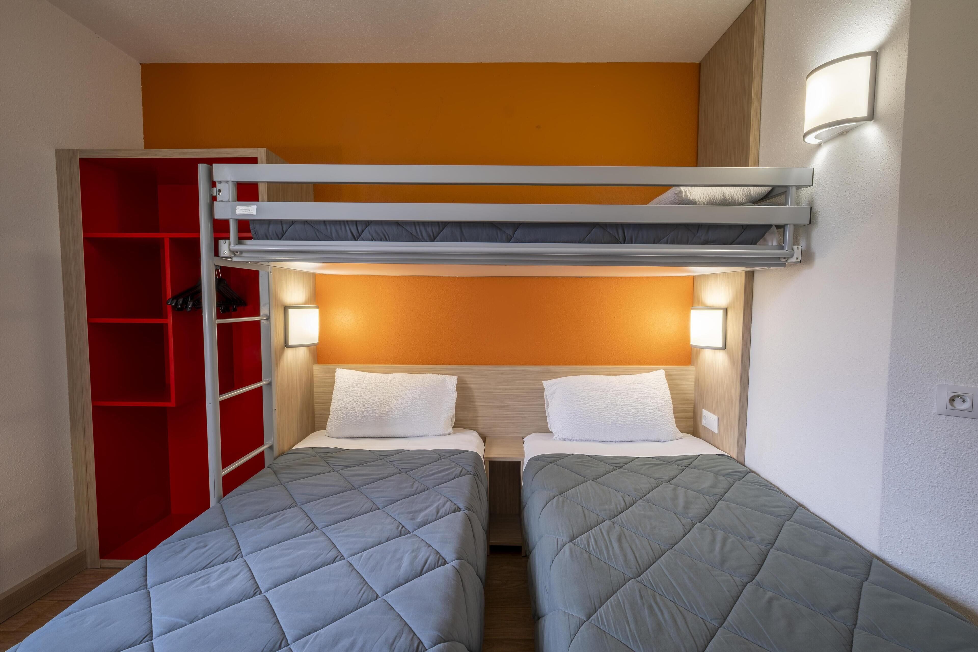 A room with two beds, a red wardrobe, and a bunk bed above.