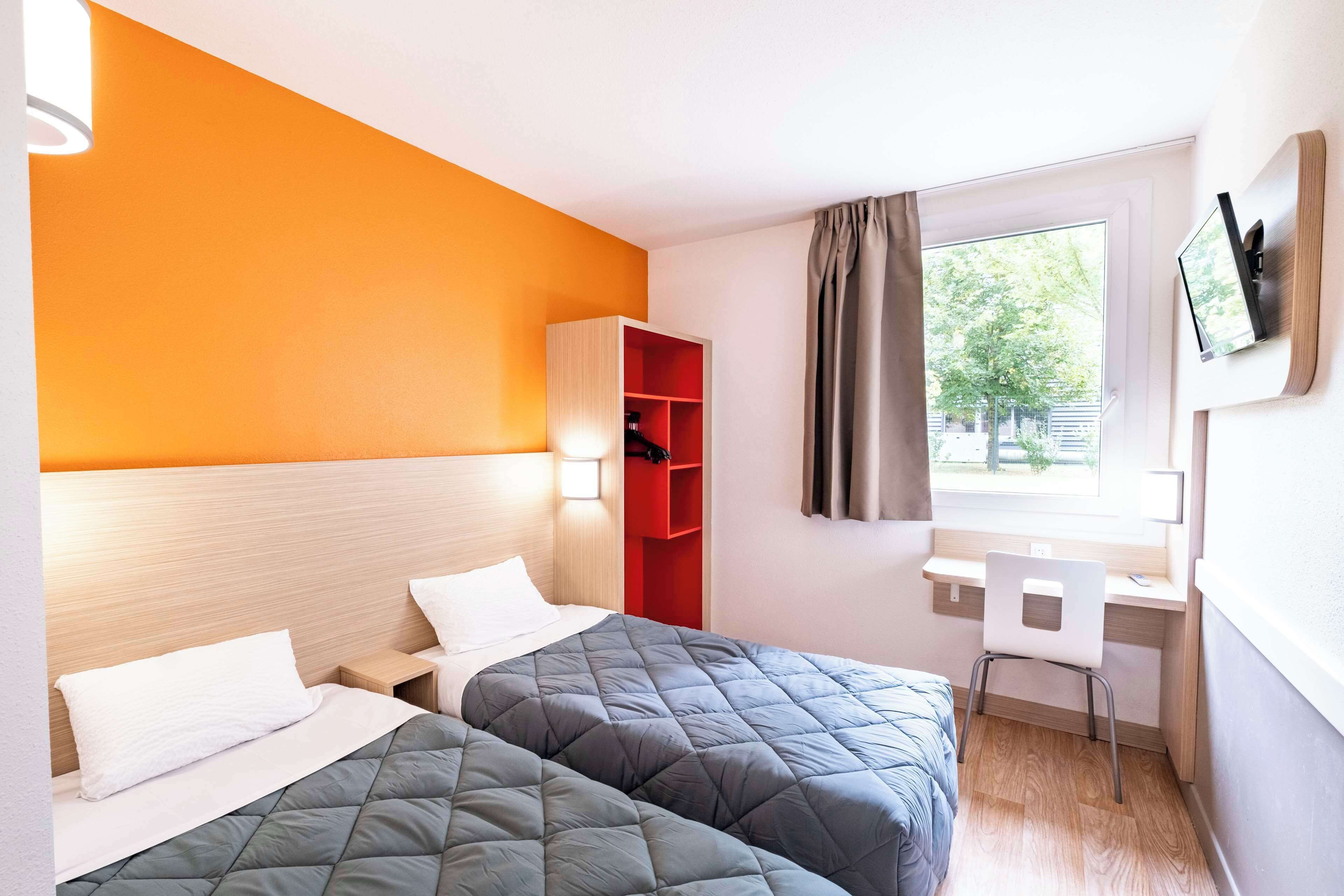 Une chambre d’hôtel avec deux lits, un bureau, une chaise, une télévision et une fenêtre avec des rideaux.