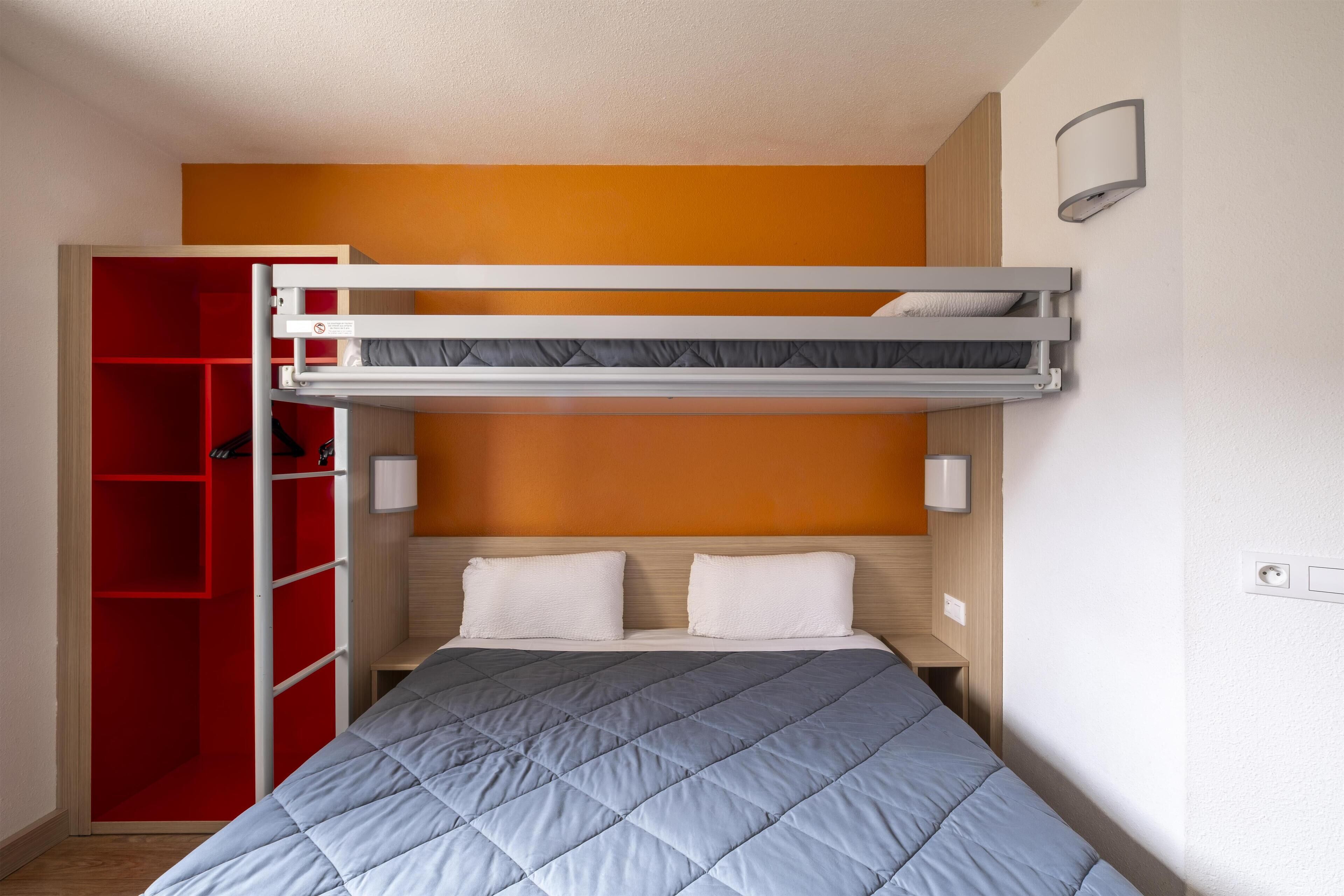 A bunk bed with a red wardrobe and a bedside table.
