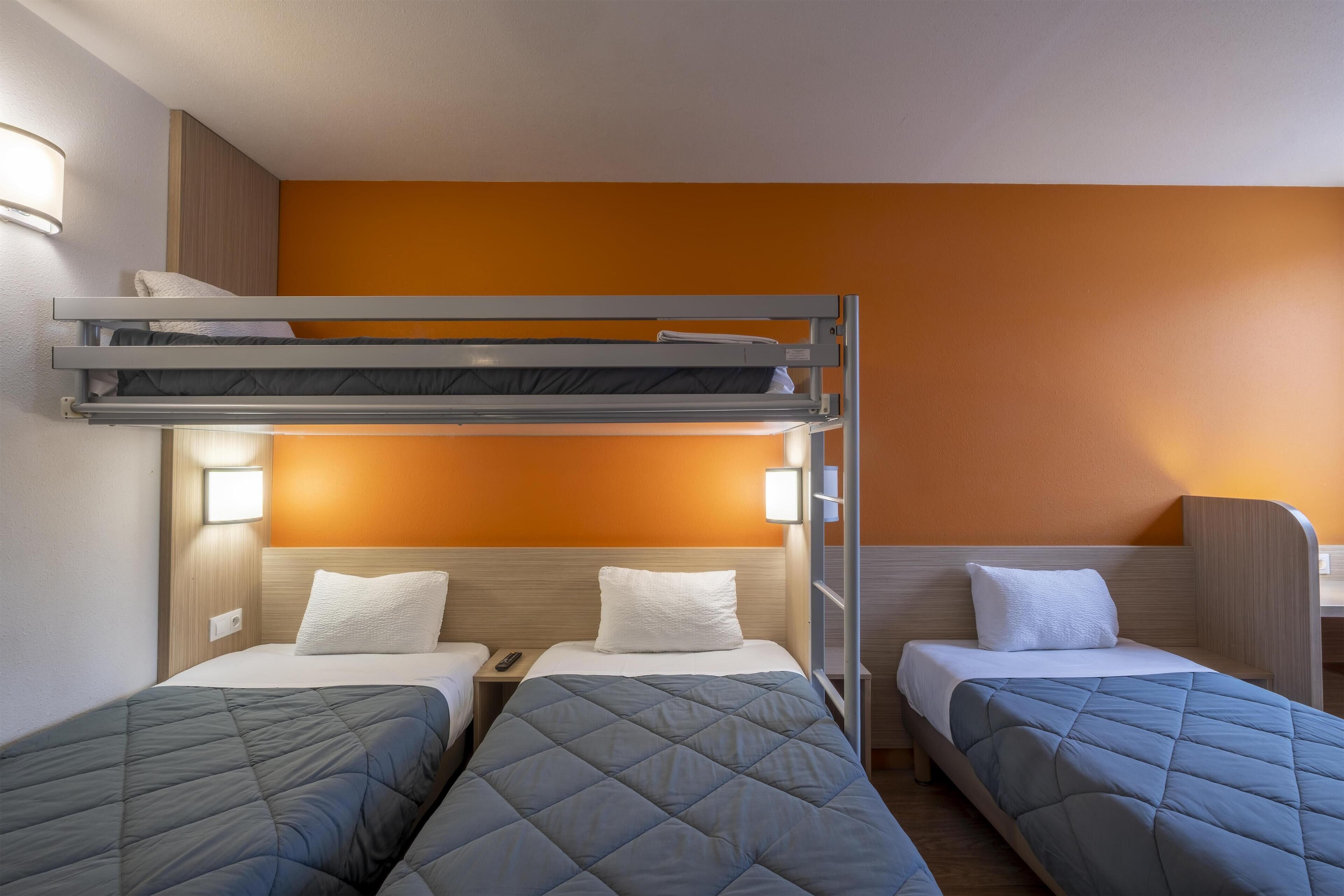 Habitación de hotel con dos camas individuales, una litera y un escritorio con silla.