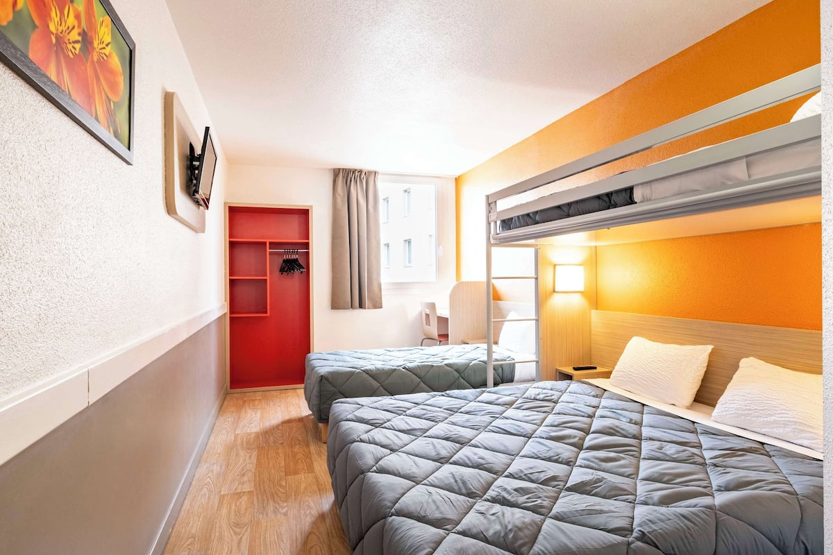 A hotel room with two beds, a red wardrobe, a desk, and a window with curtains.