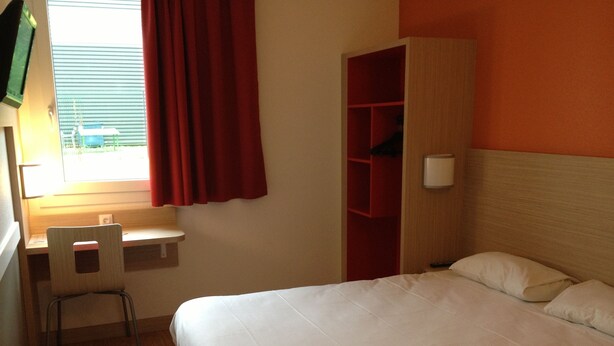 A hotel room with a bed, a desk, a chair, and a wardrobe.