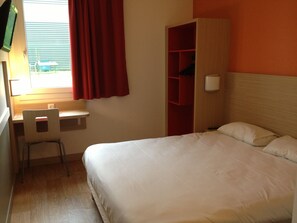 Una habitación de hotel con cama, escritorio, silla y armario.