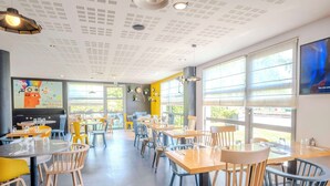 A modern restaurant with round tables and chairs, large windows, and a ceiling with a unique pattern.