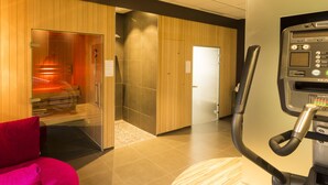 A modern hotel room with a sauna, a massage chair, and a fitness machine.