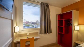 Una habitación con escritorio, silla, un mueble de almacenamiento rojo, televisor montado en la pared y ventana con cortinas.