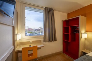 A room with a desk, a chair, a red storage unit, a TV mounted on the wall, and a window with curtains. - Premiere Classe Roissy - Aéroport CDG - Le Mesnil Amelot (Le Mesnil-Amelot)