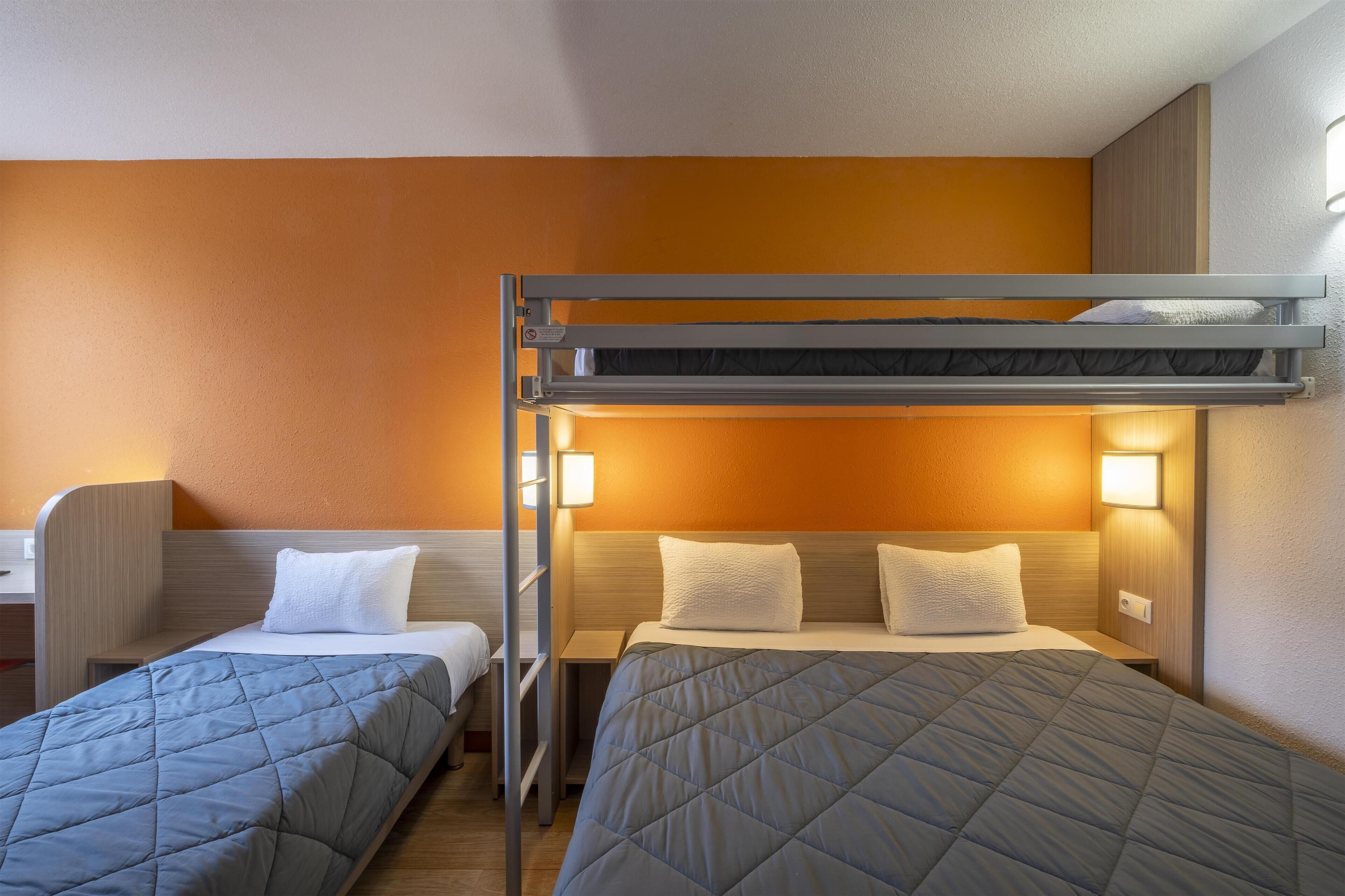 A hotel room with a bunk bed, two single beds, a desk, and bedside lamps.