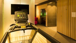A treadmill in a hotel room with a wooden floor, a television on the wall, and a red chair in the background.
