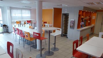 A cafeteria with white and orange tables and chairs, a vending machine, and a no-smoking sign.