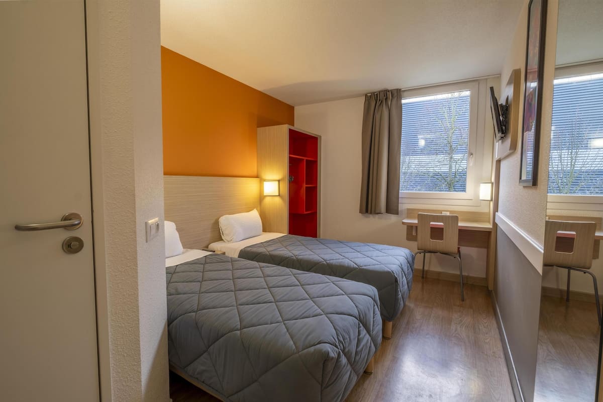 A hotel room with two beds, a desk, a chair, and a window with curtains.
