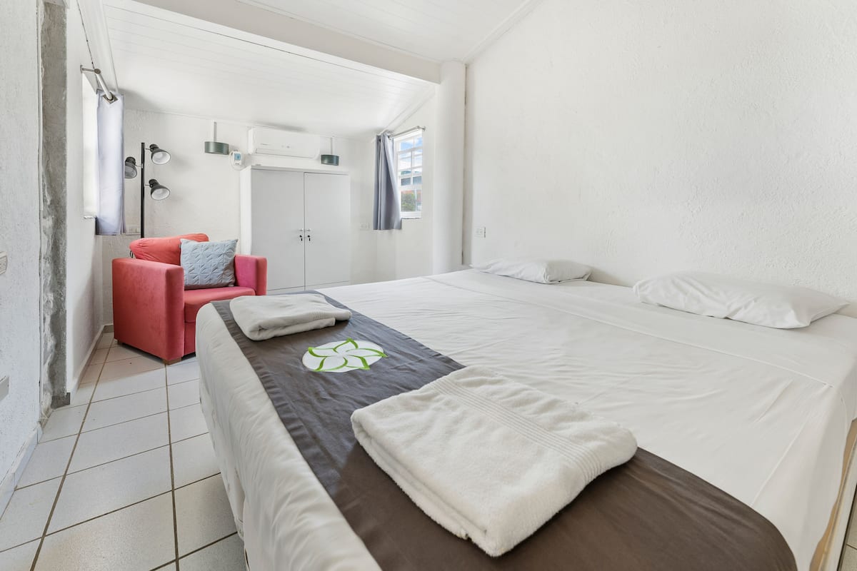 A hotel room with a bed, a red chair, a small table, and a window with curtains.