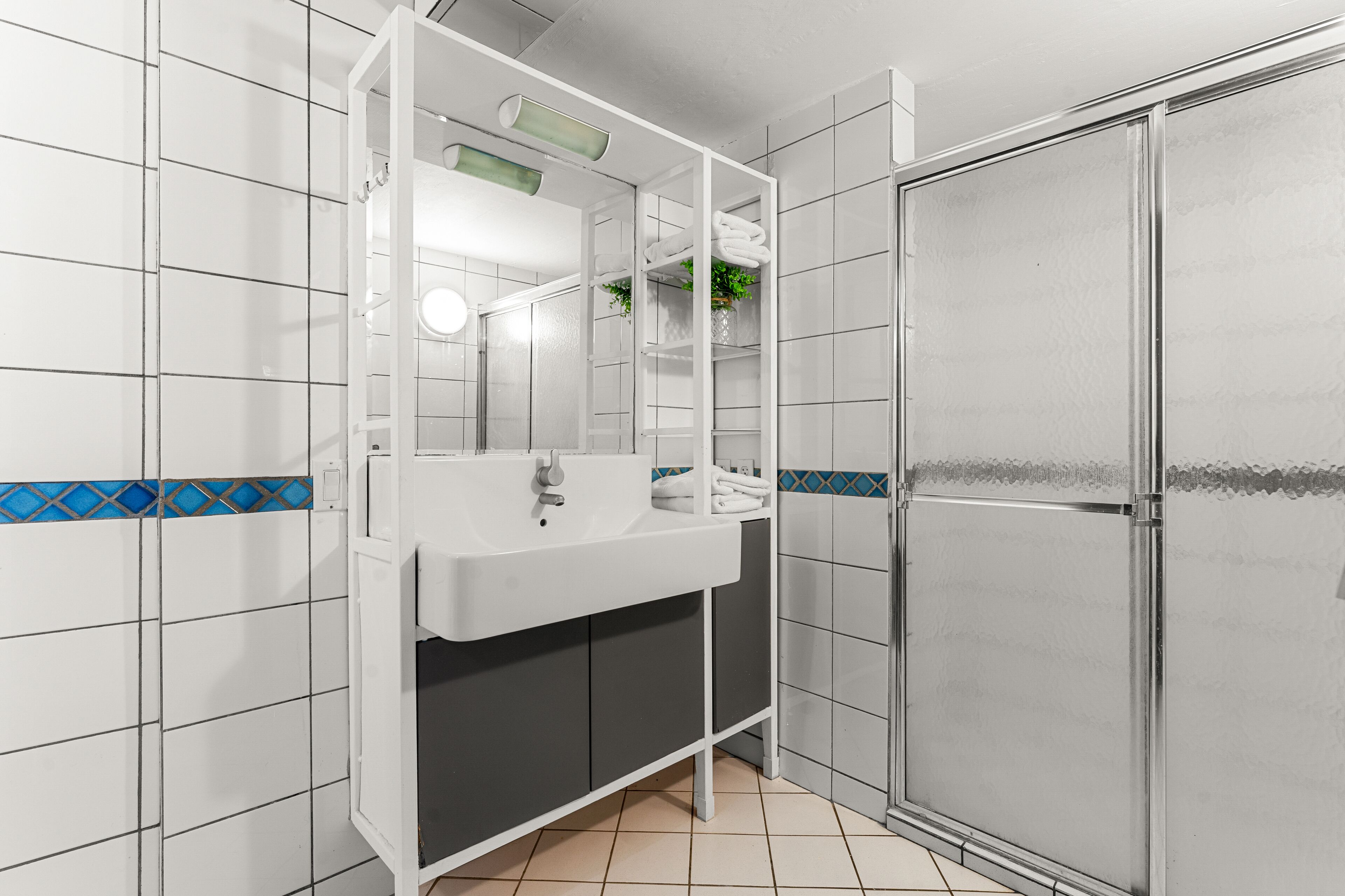 Un baño con lavamanos blanco, espejo y cabina de ducha.