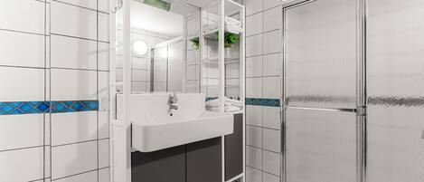 Un baño con lavamanos blanco, espejo y cabina de ducha.