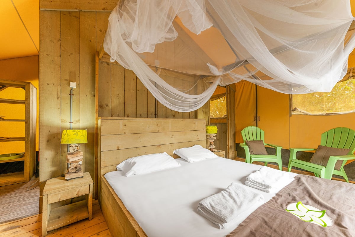 A wooden room with a bed, a nightstand, a lamp, and a chair.