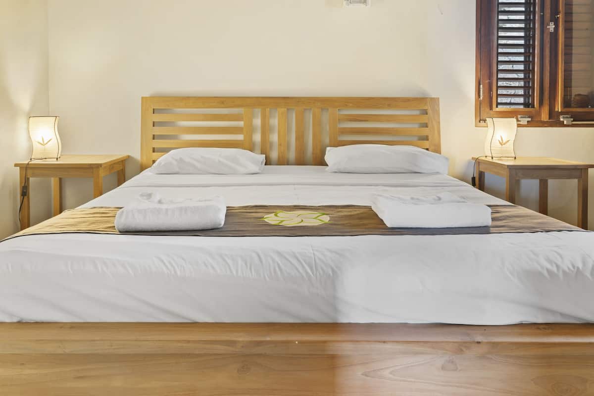 A neatly made bed with white linens and two pillows, flanked by two bedside tables with lamps.