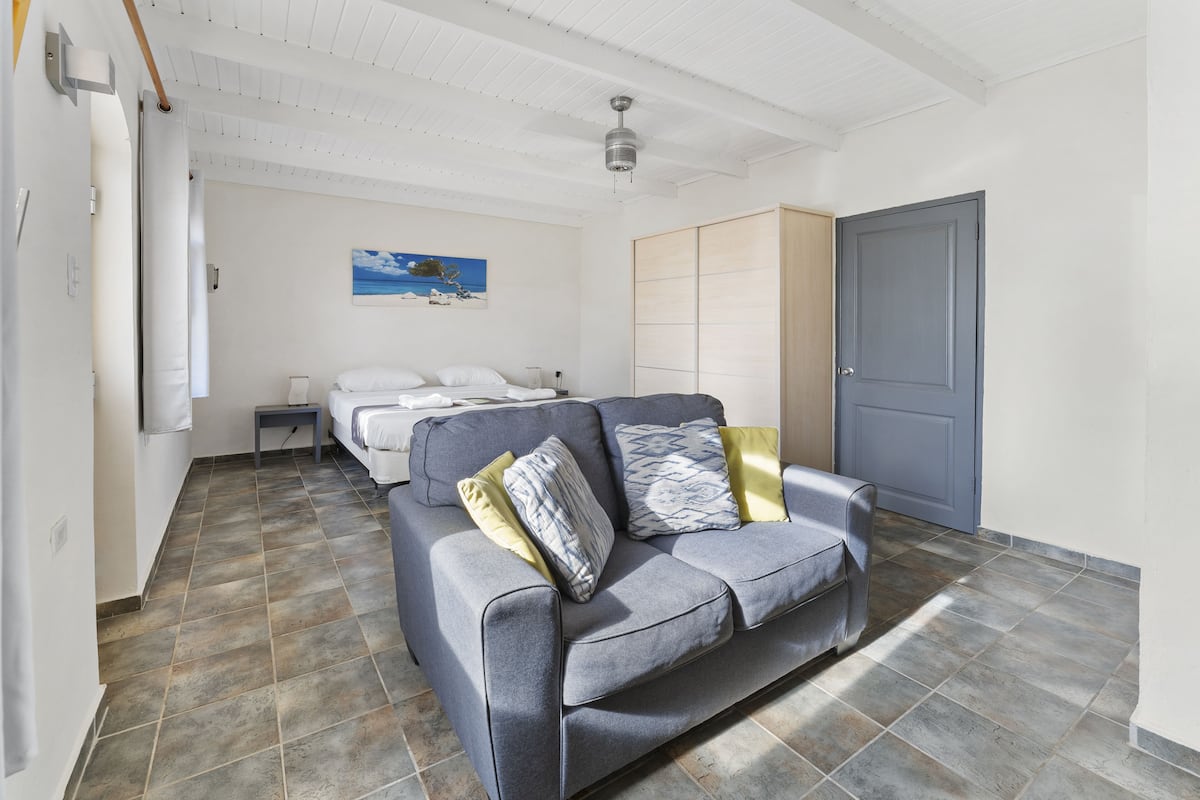 A modern bedroom with a grey sofa, a bed with white bedding, a painting on the wall, and a wardrobe.