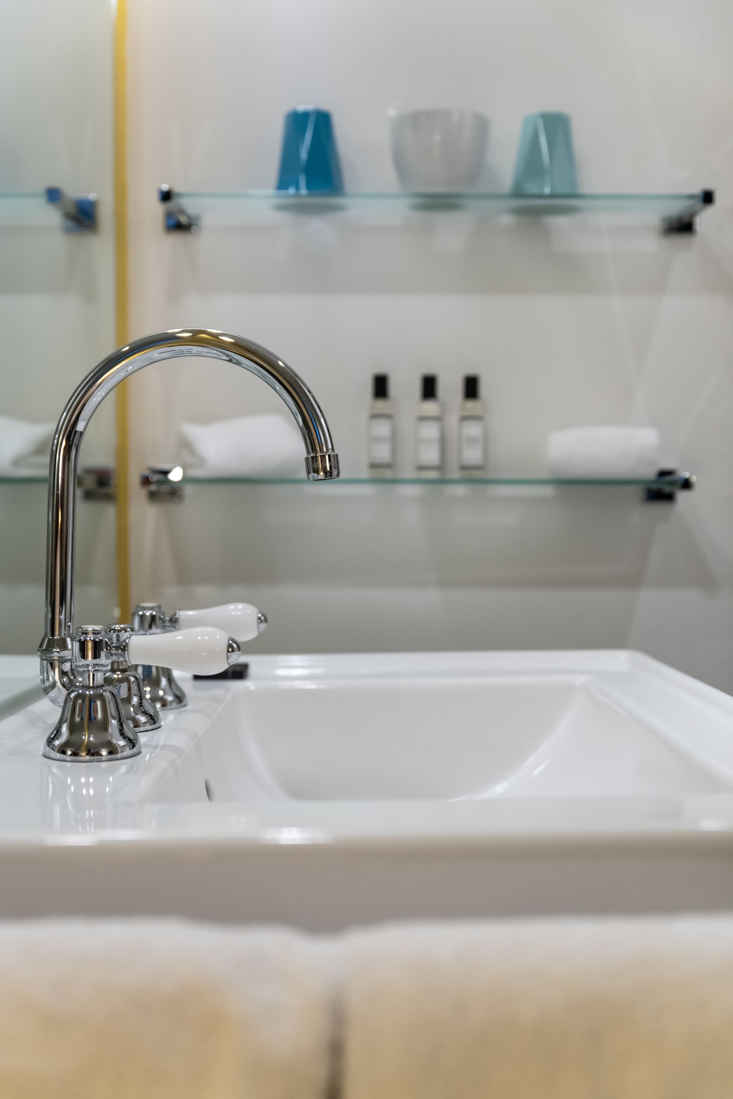 Un lavabo da bagno con un rubinetto cromato e uno scaffale in vetro sopra.