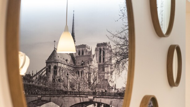 A mirror reflecting a bridge and a building, with a hanging light fixture above. - 1er Etage Marais (Paris)