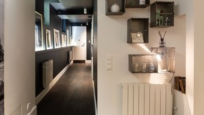 A hallway with framed pictures on the left wall, a radiator, and shelves with decorative items on the right wall. - 1er Etage Marais (Paris)