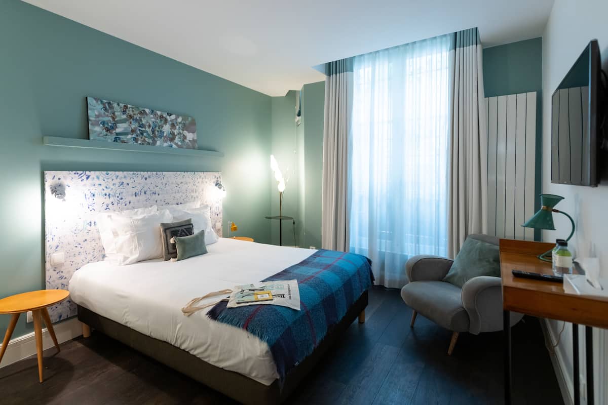 Une chambre d’hôtel bien rangée, avec un lit, un bureau, une chaise et un téléviseur fixé au mur.