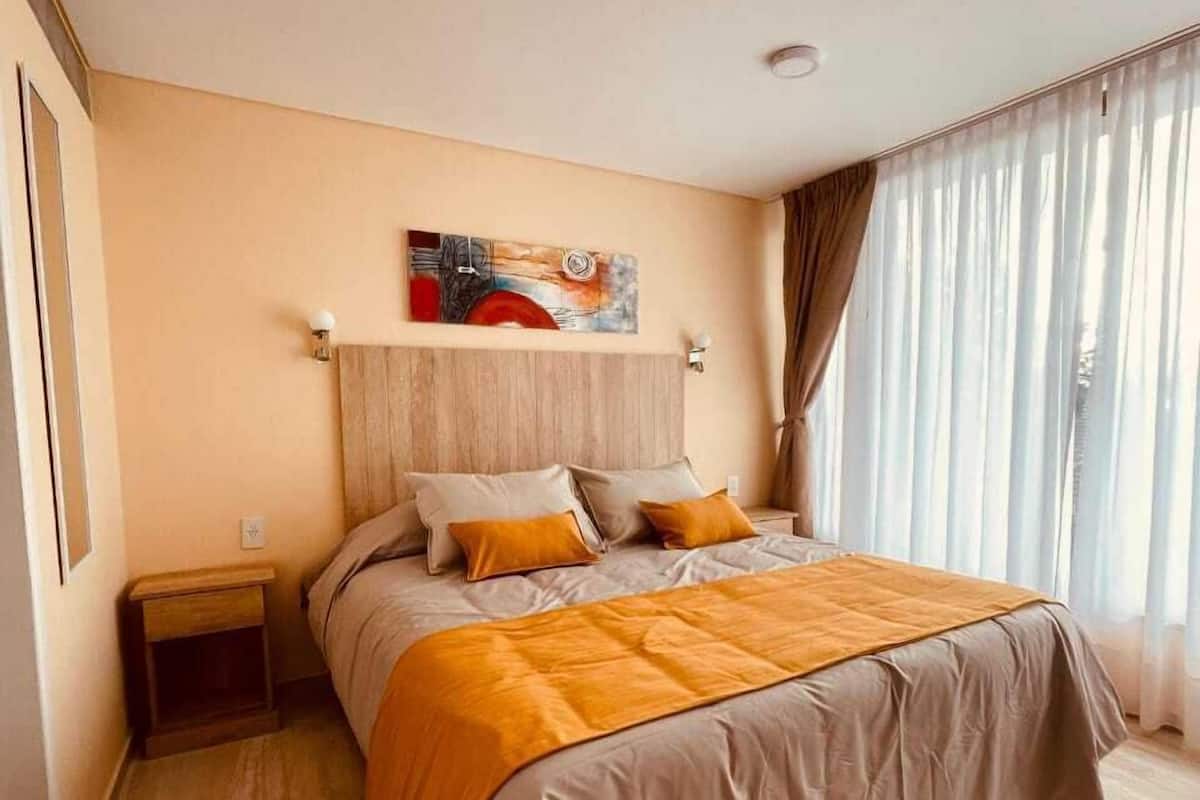 Une chambre moderne avec un grand lit, une tête de lit, une table de chevet et une fenêtre avec des rideaux.