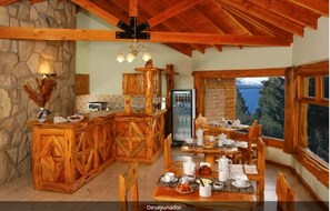 A rustic kitchen with wooden cabinetry, a stone wall, and a dining area with a table set for breakfast.