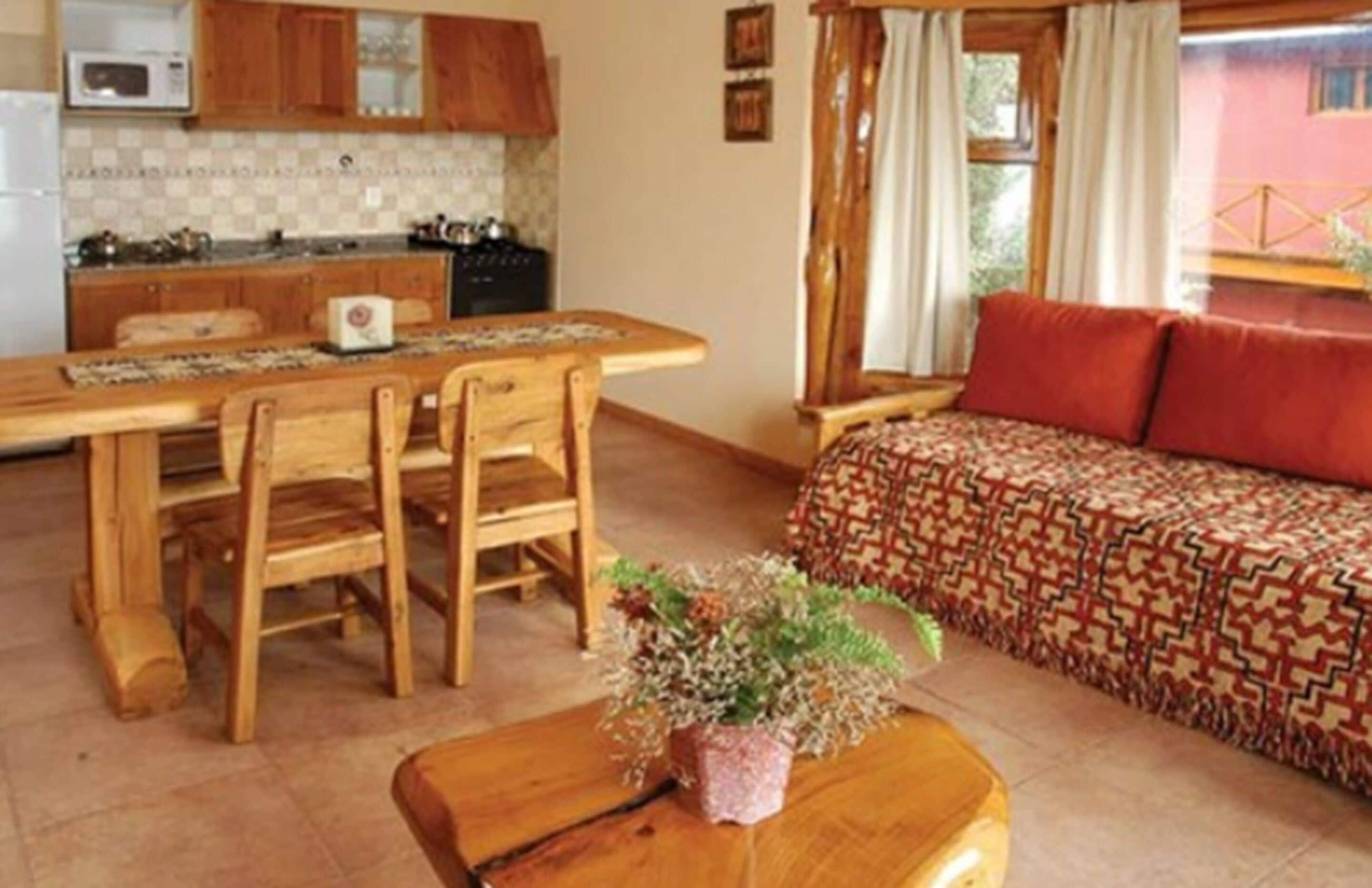 Une pièce chaleureuse avec une table à manger en bois, des chaises, un canapé recouvert d’un tissu à motifs et une petite table en bois sur laquelle est posée une plante.