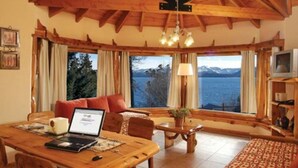 Una habitación acogedora con techo de madera, una mesa de comedor con una computadora portátil, un sofá y un televisor.