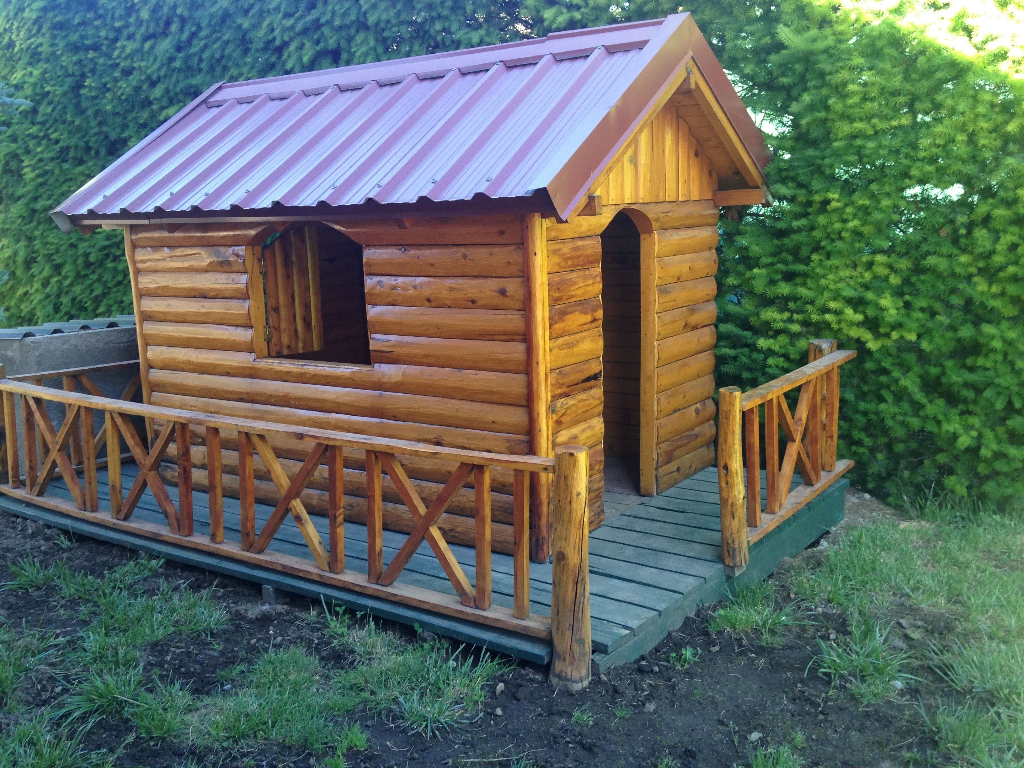 A wooden cabin with a metal roof, a porch, and a small window.