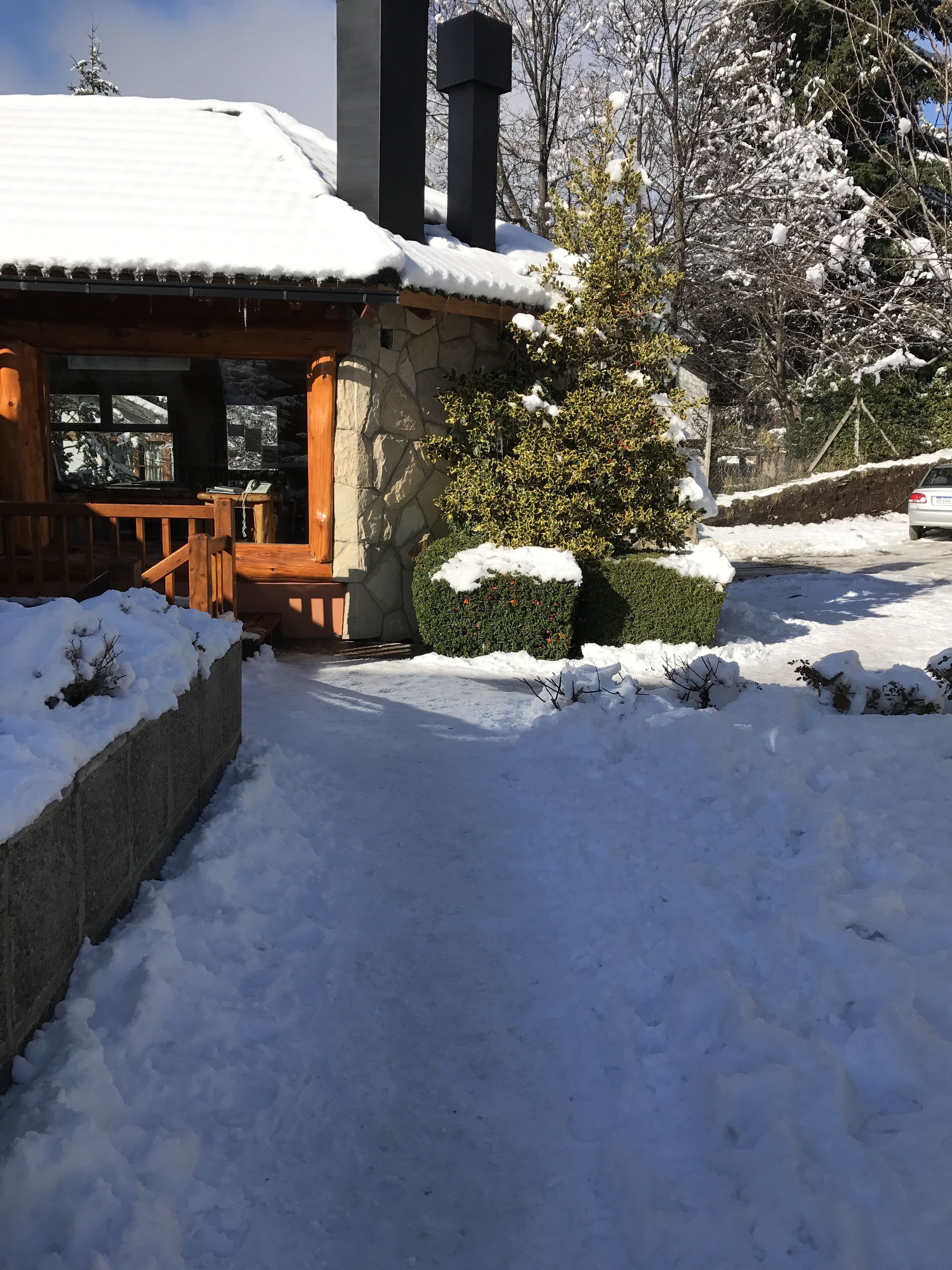Ein mit Schnee bedecktes Chalet mit Steinaußenwand, einer Holzdachterrasse und einer Steinmauer.