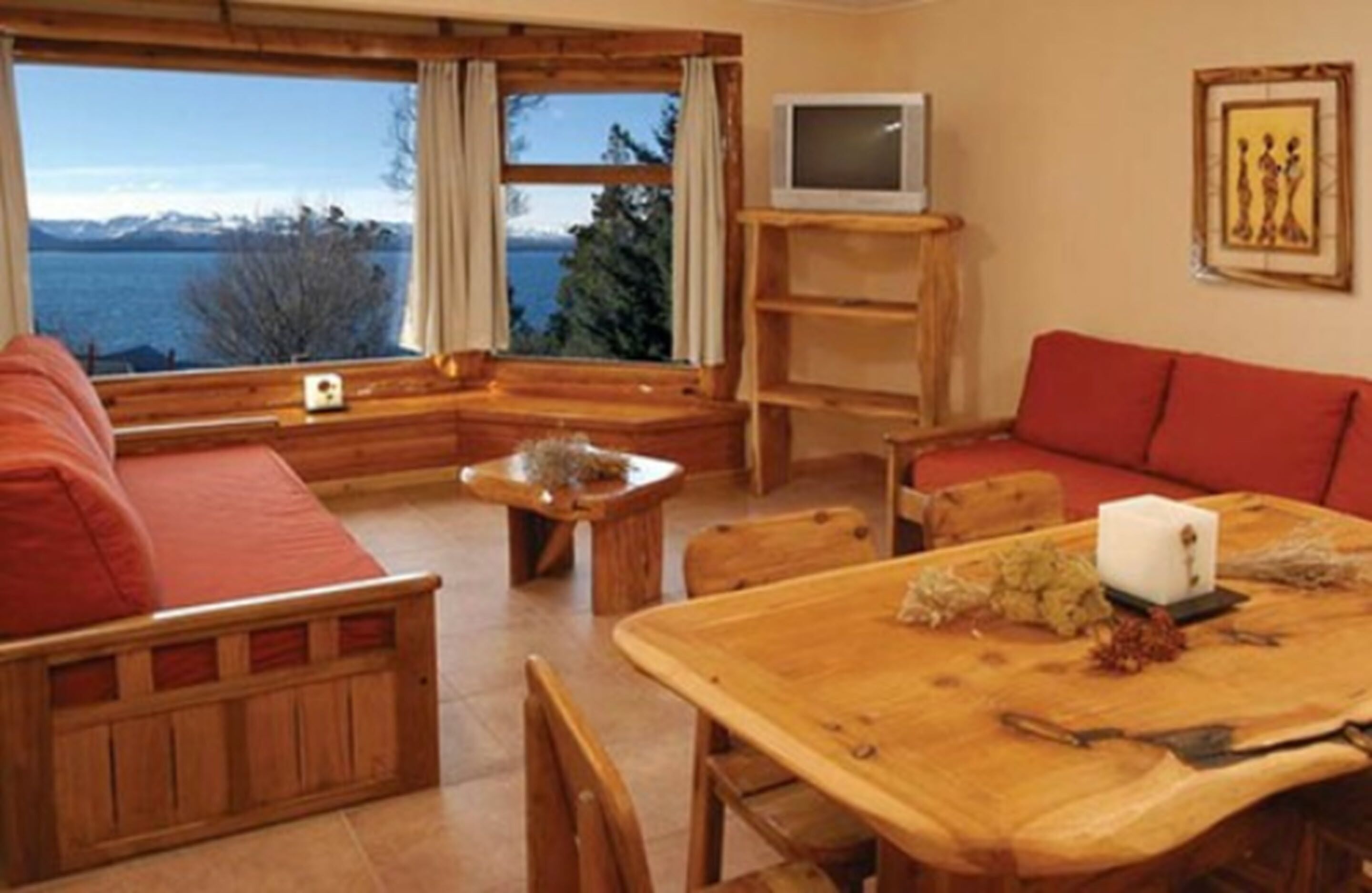 Ein gemütliches Blockhaus-Interieur mit einem Holzesstisch, einem roten Sofa und einem Fernseher auf einem Regal.