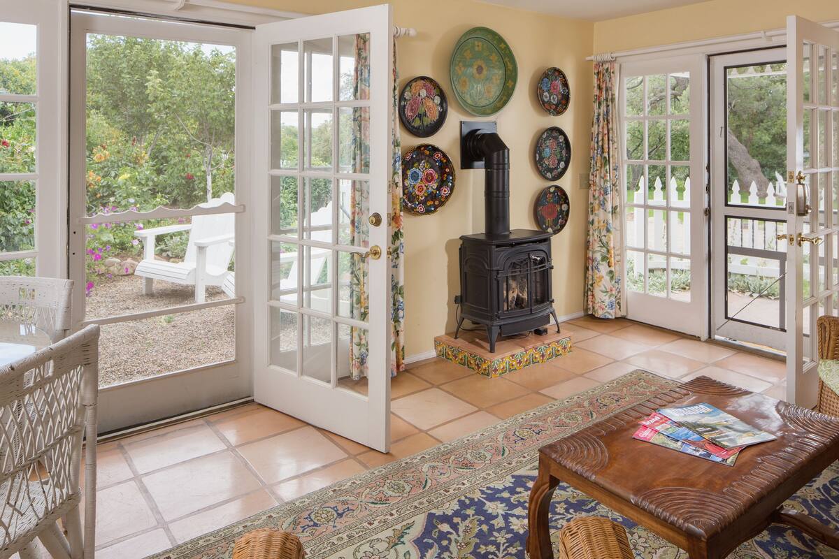 Une pièce chaleureuse avec une cheminée, une table à manger et une vue sur le jardin grâce à des portes ouvertes.