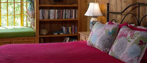 Una habitación acogedora con una estantería de madera, un banco con cojines verdes y una cama con una manta roja y almohadas estampadas.