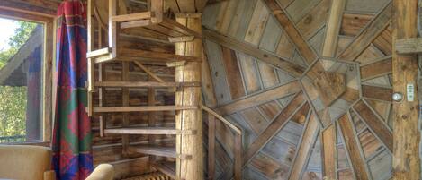 A wooden cabin interior with a spiral staircase, a round table, and a rustic fireplace.