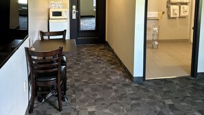 A hotel room with a dining area, a microwave, a door leading to another room, and a bathroom with towels and a toilet paper holder. - Midland Inn & Suites (Midland)