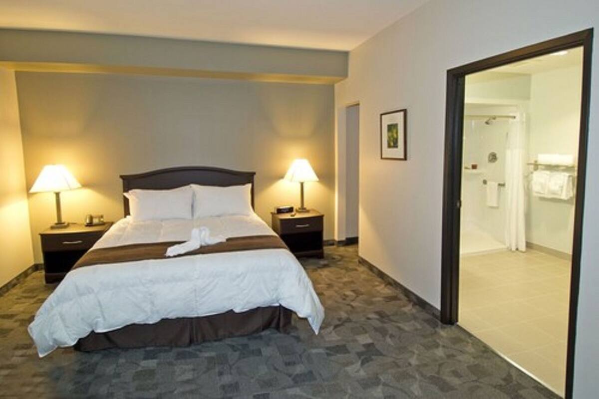 Una habitación de hotel con una cama, dos lámparas de noche, una bata y una puerta que da a un baño.