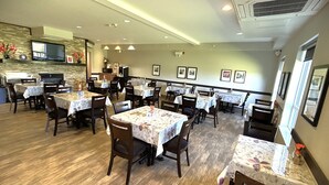A restaurant with multiple tables and chairs, a kitchen area, and framed pictures on the walls. - Midland Inn & Suites (Midland)