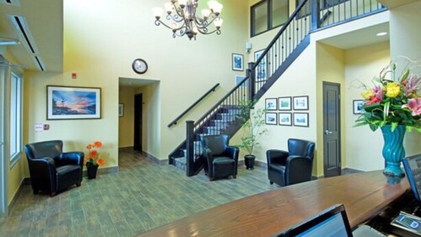A reception area with a wooden reception desk, black leather chairs, a chandelier, a staircase, and framed pictures on the walls. - Midland Inn & Suites (Midland)