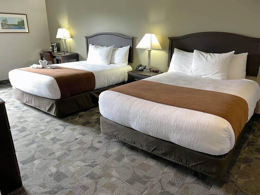 Hotellihuoneessa on kaksi sänkyä, joissa on ruskeat päätyosat ja valkoiset vuodevaatteet. Huoneessa on myös kaksi yöpöytää, joissa on lamput, seinällä on kehystetty kuva ja lattialla on matto.