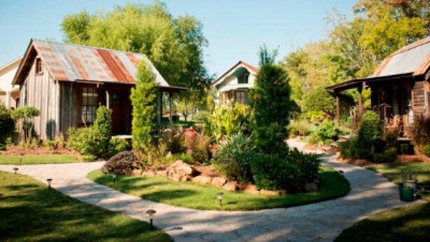 A rustic cabin-style building with a metal roof, surrounded by well-maintained landscaping and a clear sky.