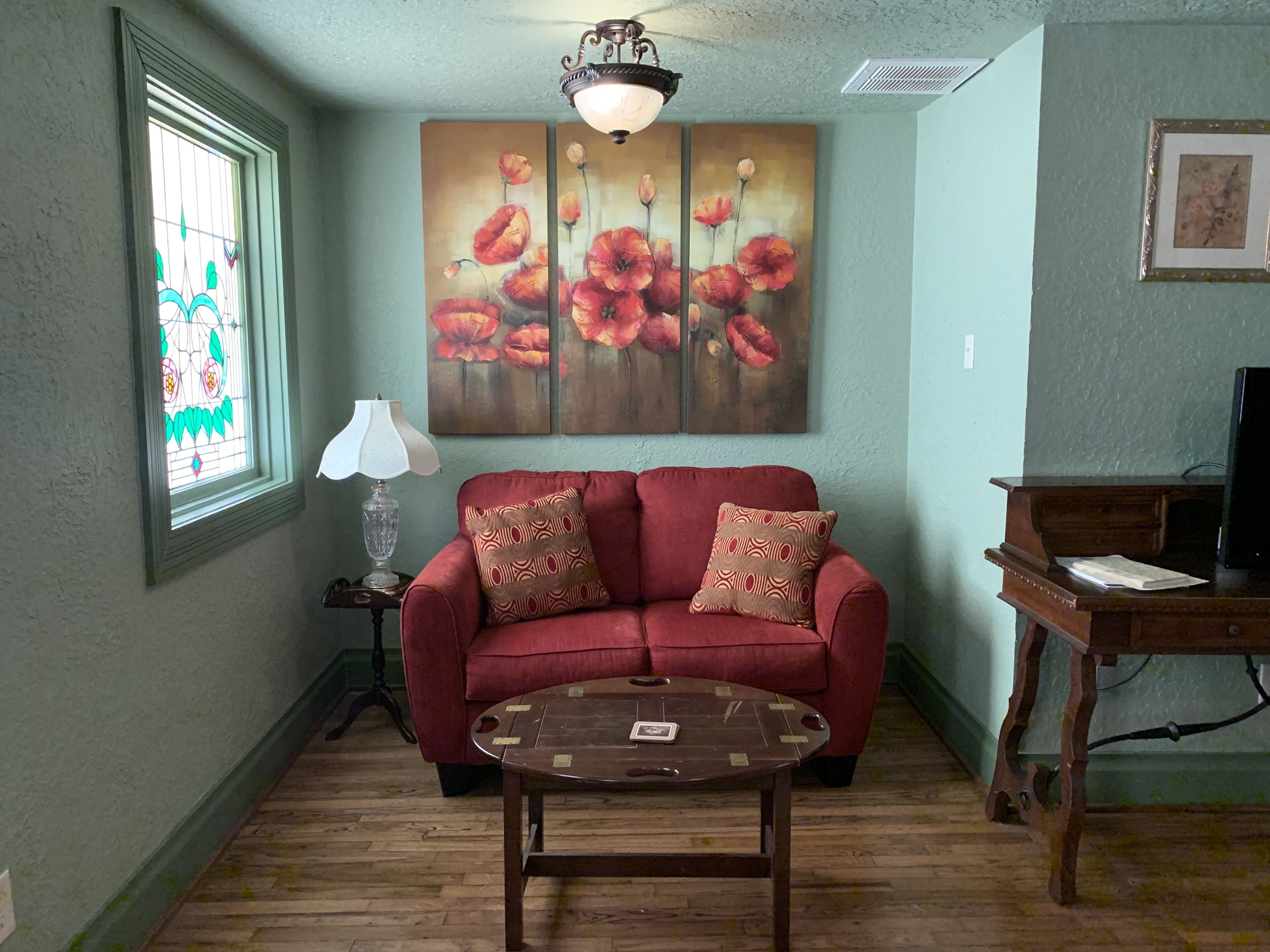 A living room with a red sofa, a wooden coffee table, a lamp, and a painting of flowers on the wall.