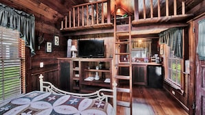 A cozy cabin interior with a loft bedroom, a dining area, and a kitchen.