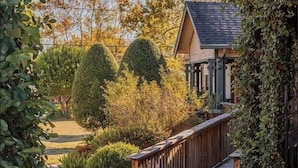 A wooden deck leading to a house with a sloped roof, surrounded by well-maintained bushes and trees.