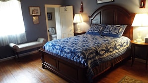Une chambre à coucher avec un grand lit, un banc, une porte et une table de chevet avec une lampe.