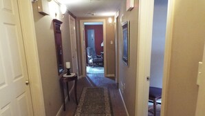 Un couloir avec un tapis à motifs, une petite table sur laquelle est posée une bougie, et une chaise au fond.