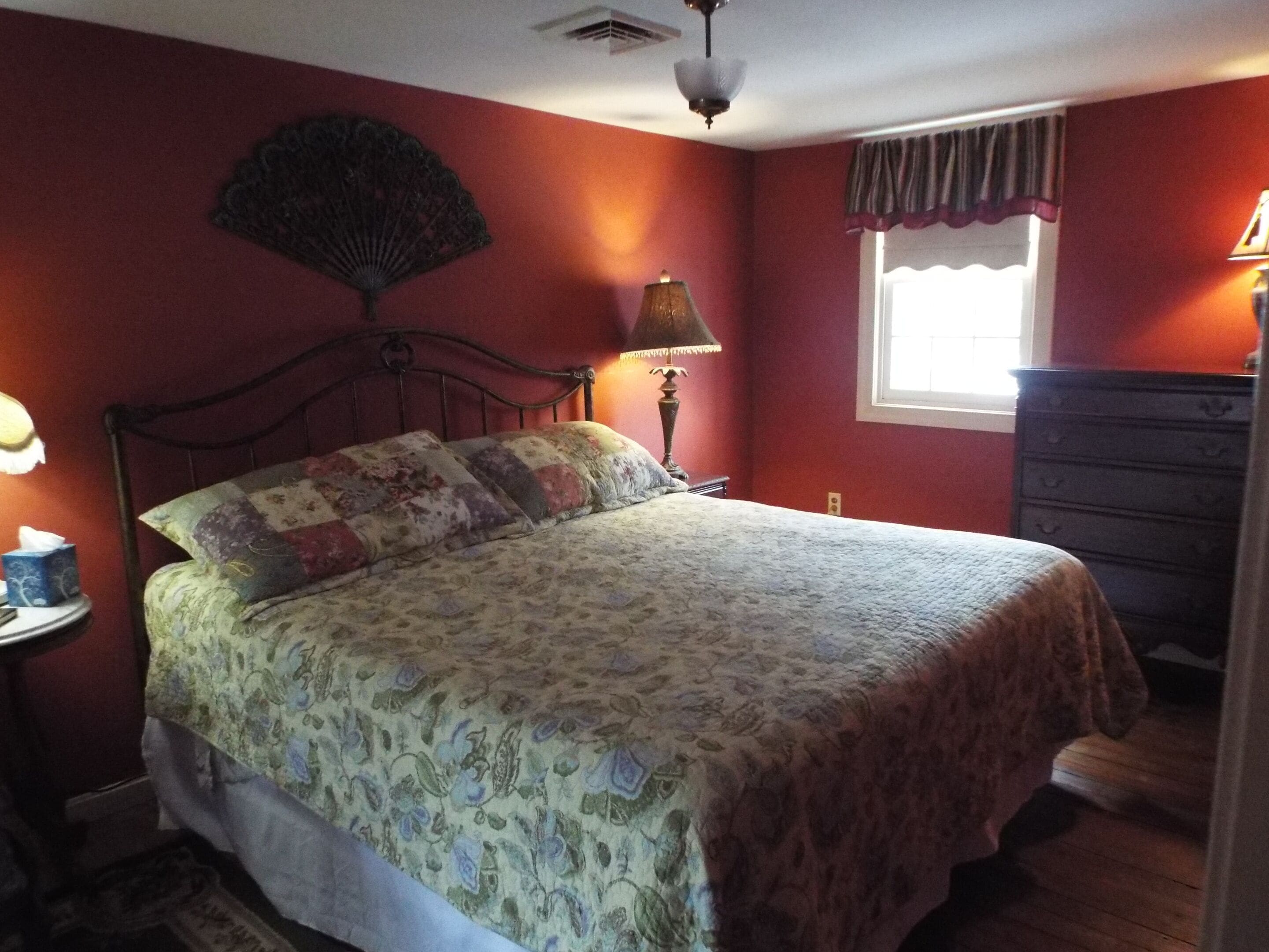 A bedroom with a bed, a dresser, a nightstand, a lamp, and a window with curtains.