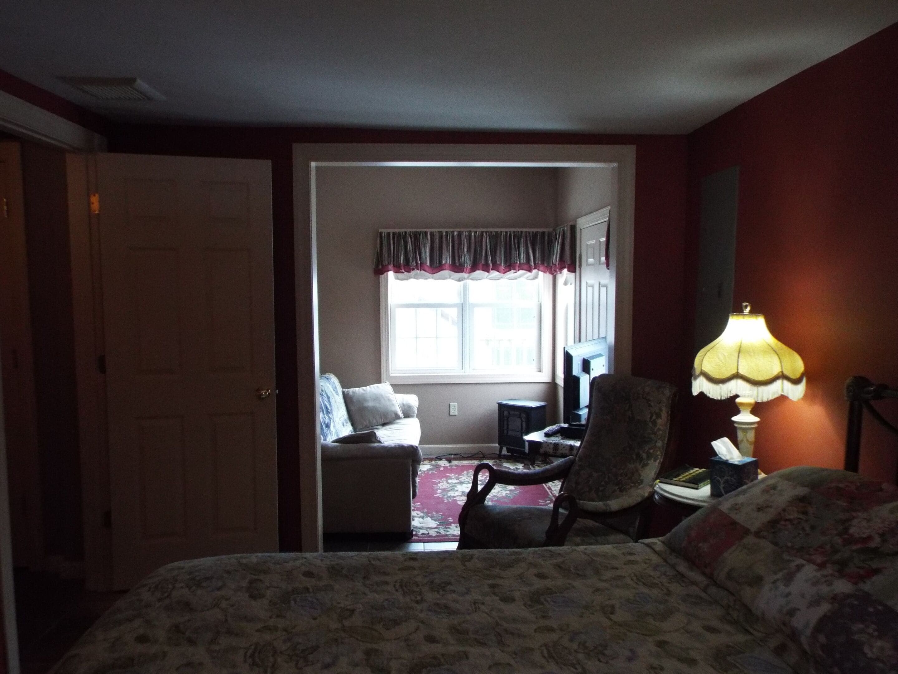 Una habitación de hotel con una cama, una silla, un escritorio, una lámpara y una ventana con cortinas.