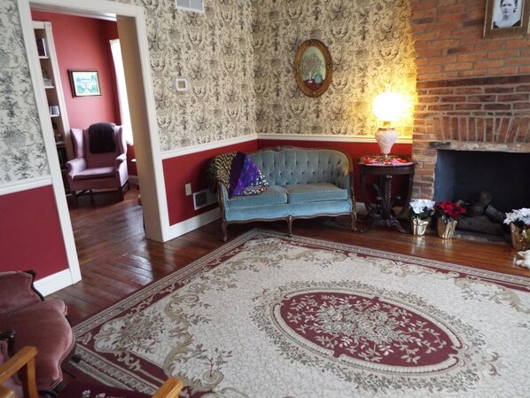 A living room with a blue sofa, a patterned rug, a fireplace, and a red wall. - The Tillie Pierce House Inn (Gettysburg)